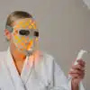 a woman wearing an led face mask and holding a remote control