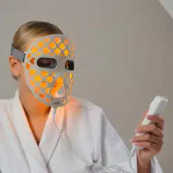 a woman wearing an led face mask and holding a remote control